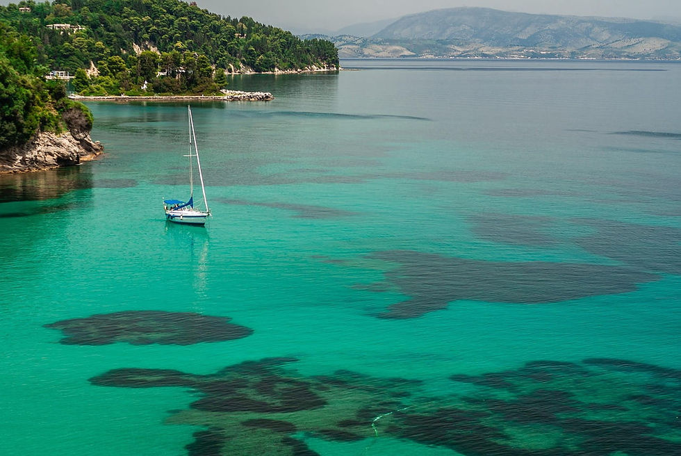 Segelboot auf türkisfarbenem, ruhigem Meer vor grüner Küste und Bergen.