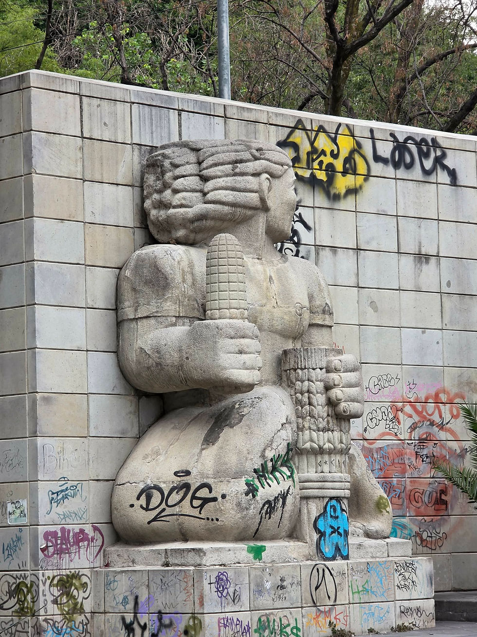 Graffiti-beschmierte Steinfigur mit Säule an gekachelter Wand in Mexiko-Stadt, im Park vor Bäumen.