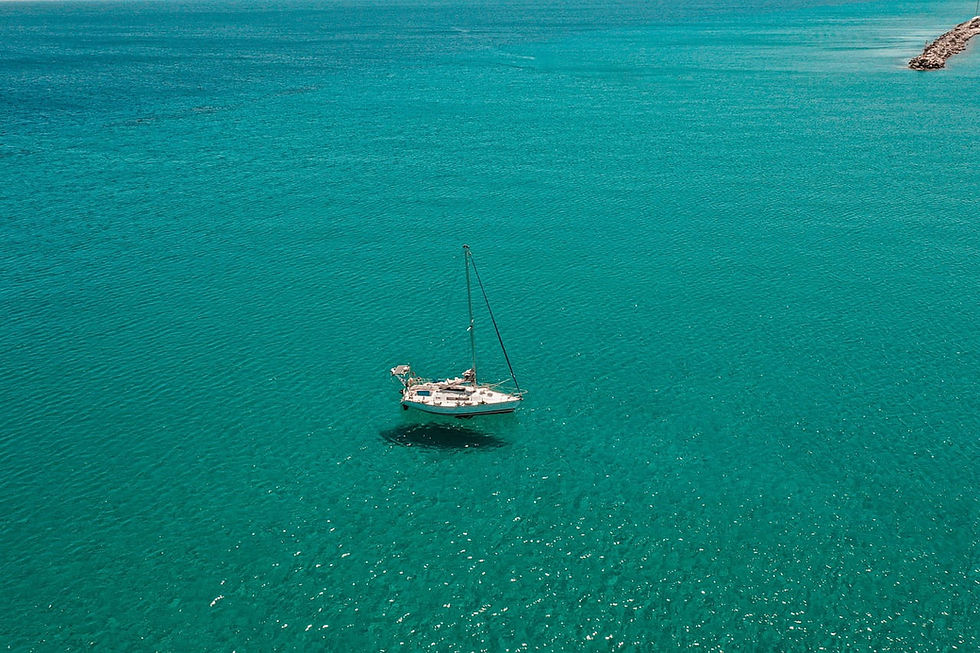 Segelboot auf türkisfarbenem Meer, nahe einer Felsenbucht; ruhige, sonnige Wasserfläche auf Kos.