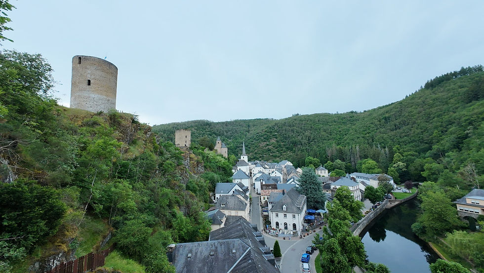 Mittelalterlicher Rundturm über grünem Tal mit Dorf, Kirche und Fluss, umgeben von bewaldeten Hügeln.