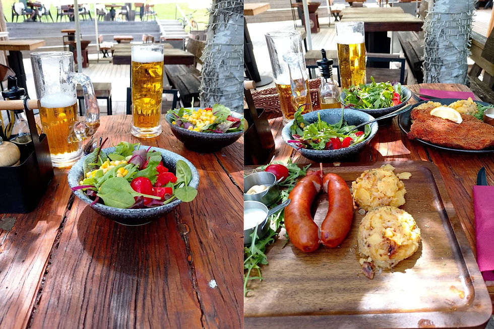 Rustikales Biergarten-Essen im Freien: zwei Biergläser, Salate, Bratwurst, Schnitzel und Kartoffelbeilagen auf Holztisch.