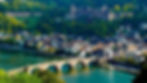 Heidelberger Altstadt mit Alter Brücke, Neckar und Schloss auf dem bewaldeten Hügel, sonnig und farbenfroh.