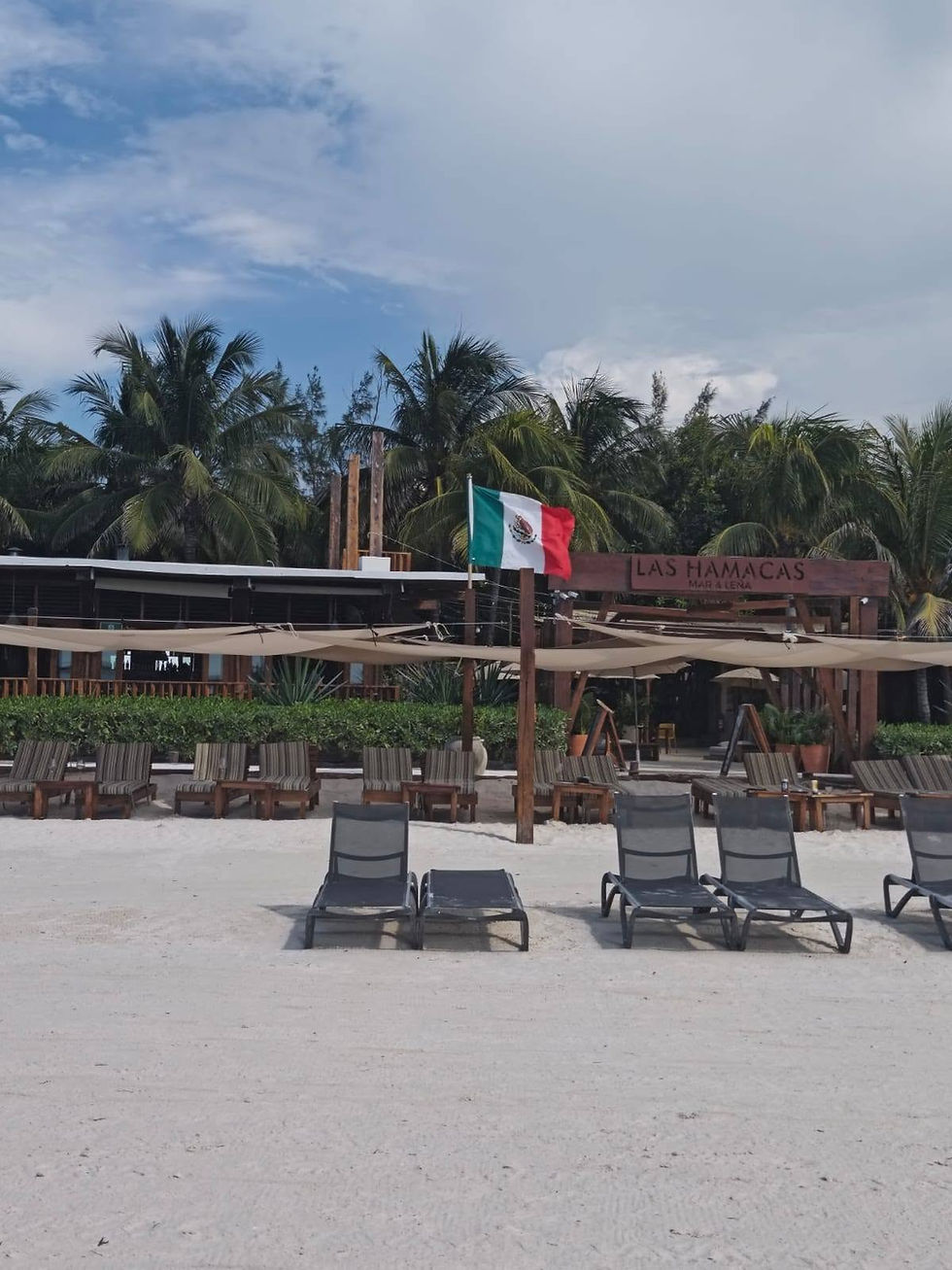 Strandclub mit Liegen vor Palmen, mexikanischer Flagge und Schild Las Hamacas auf der Insel Holbox. Ruhige, sonnige Atmosphäre.