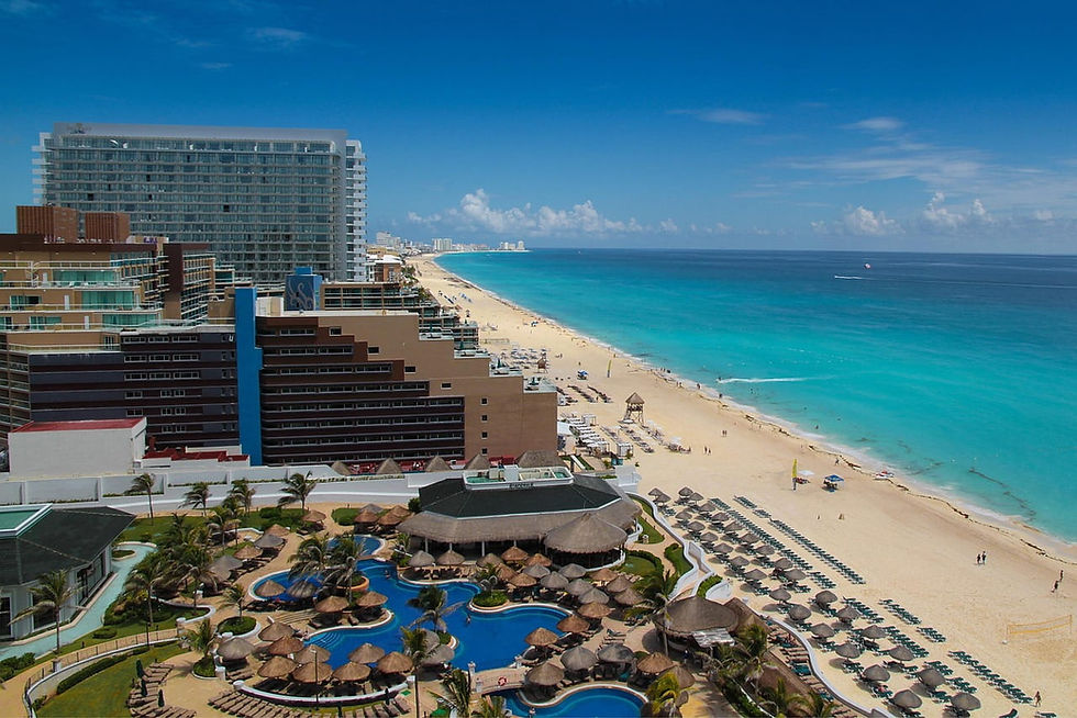 Blick auf Strandresort mit Hotels, Pools und Sonnenschirmen am türkisblauen Meer von Cancun unter klarem Himmel.