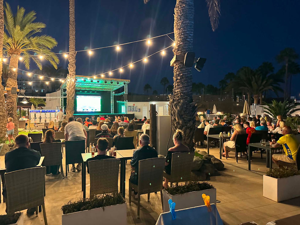 Abendliches Public Viewing im Palmenhof: Viele Menschen sitzen vor großer Leinwand unter Lichterketten und Palmen auf Gran Canaria
