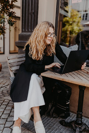 „Person mit langen Haaren sitzt draußen an einem Tisch und arbeitet konzentriert am Laptop; ruhige Szene einer persönlichen Online-Beratung.“