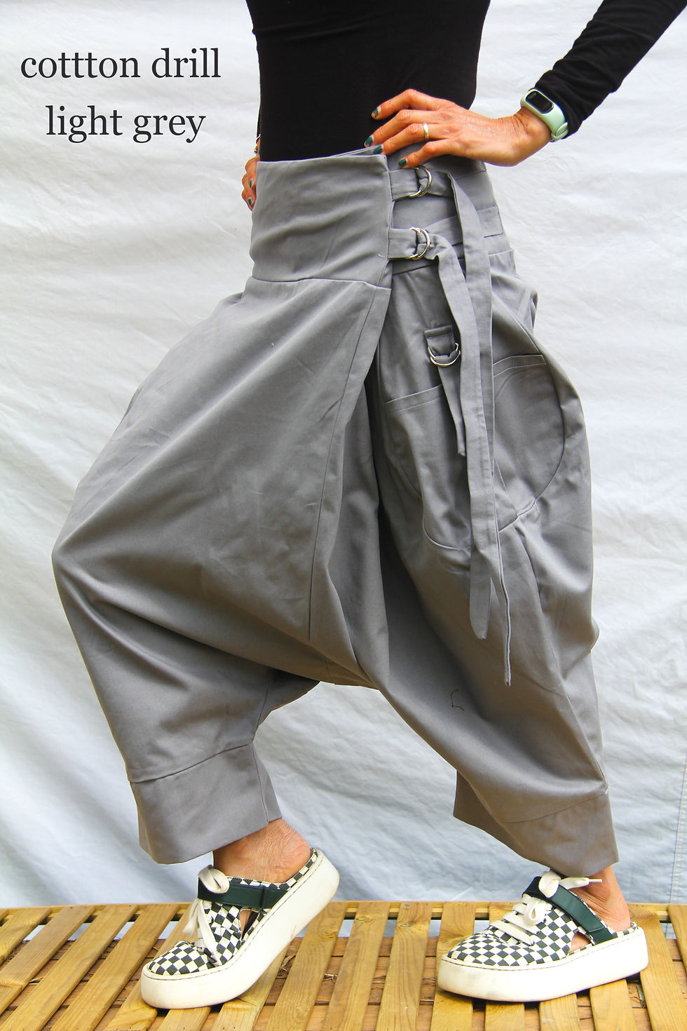 Thumbnail: waist down view of a model wearing a structured plain cotton trousers with a modern take on fisherman pants