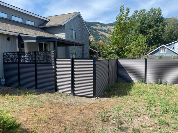 a corrugated galvanized metal fence with black metal posts surrounds a home in vernon bc