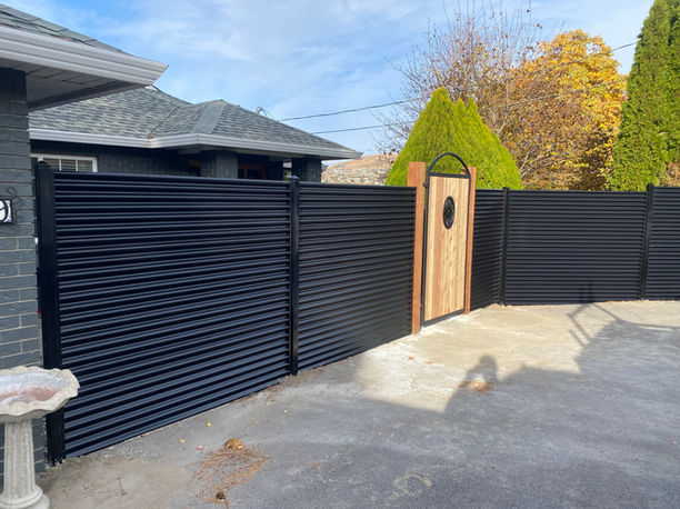 black corrugated metal fence with metal posts and a cedar custom gate built by blue rhino fence in vernon bc