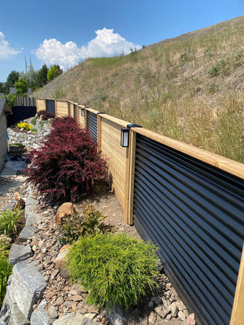 five foot privacy fence made of black corrugated metal with wood posts alternating with panels of cedar by blue rhino fence in vernon