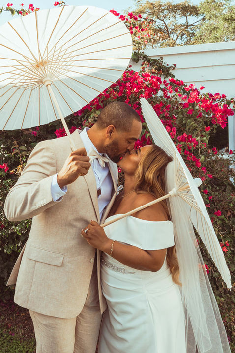 A bride and groom kissing while holding white umbrellas.