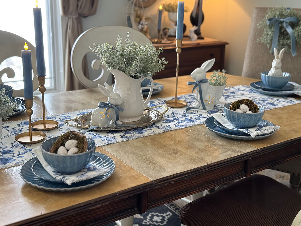 Elegant table setting with blue candles, bunny decorations, and greenery. Blue patterned plates, and nests with eggs complete the decor.