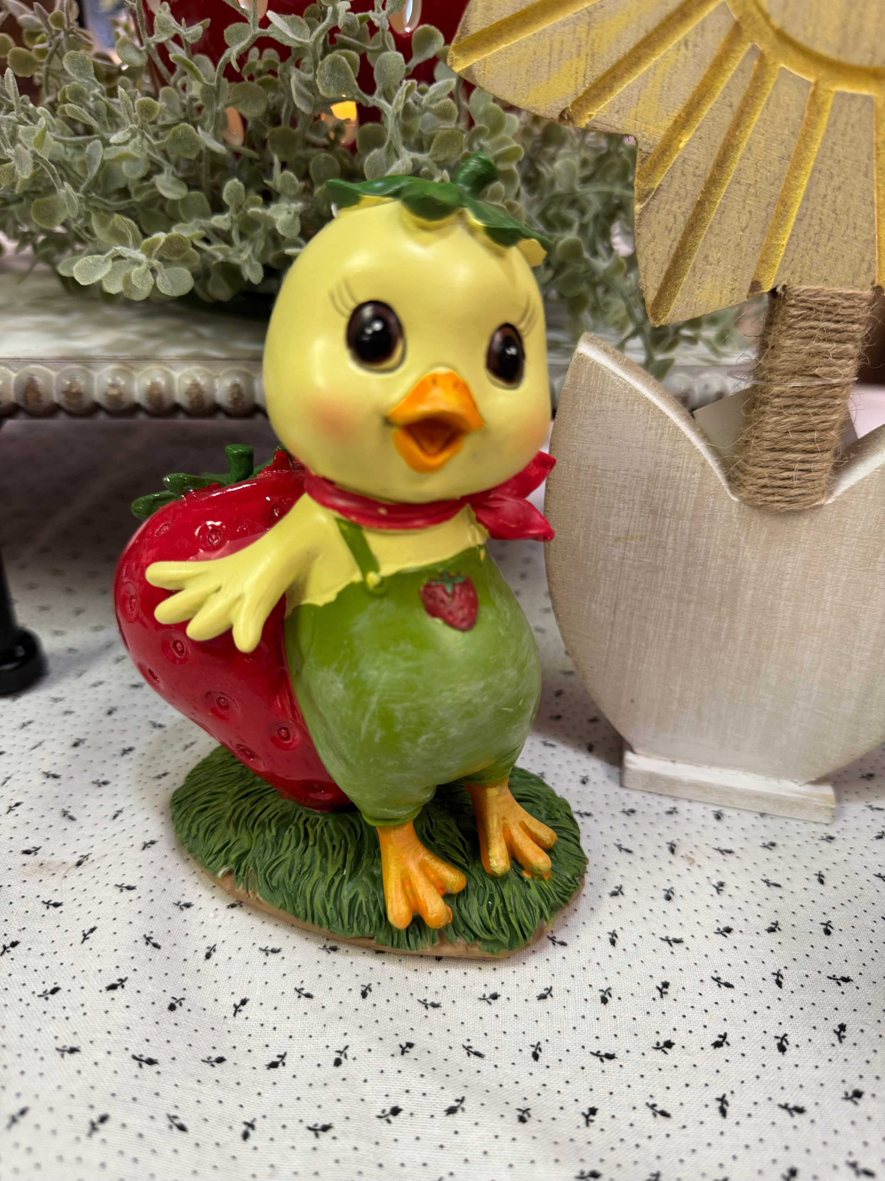 5.5" resin figurine, yellow chick wearing a green jumpsuit with a strawberry patch, chick is leaning on a big strawberry