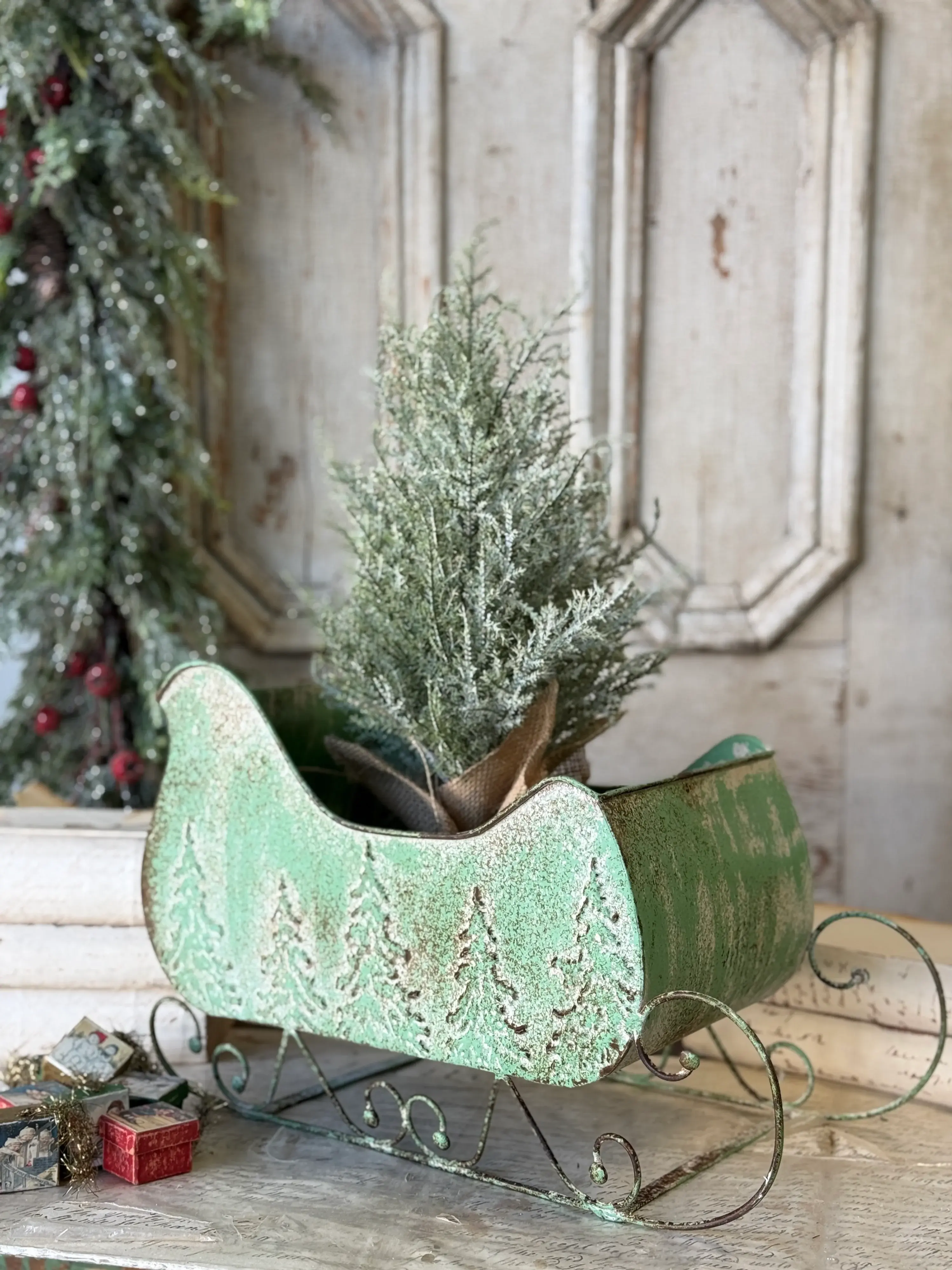 18 inch Skyscape metal Christmas sleigh with distressed green finish, embossed evergreen trees and decorative scroll runners.