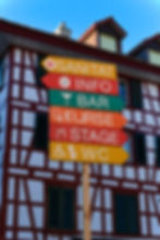 Signpost at a large festival. A half-timbered house in the background.