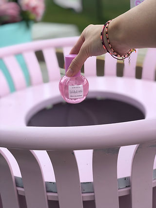 A hand holding a serum bottle over a pink garbage bin.