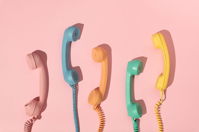Vijf retro telefoonhoorns in pastelkleuren aan een roze muur, van links naar rechts in roze, blauw, oranje, groen en geel – vintage communicatieconcept met kleurrijke esthetiek