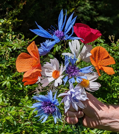 An image of a bunch of beautiful white, orange, red, blue and white flowers of various shapes from the crêpe paper flower workshop at The Oast Studio, East Sussex