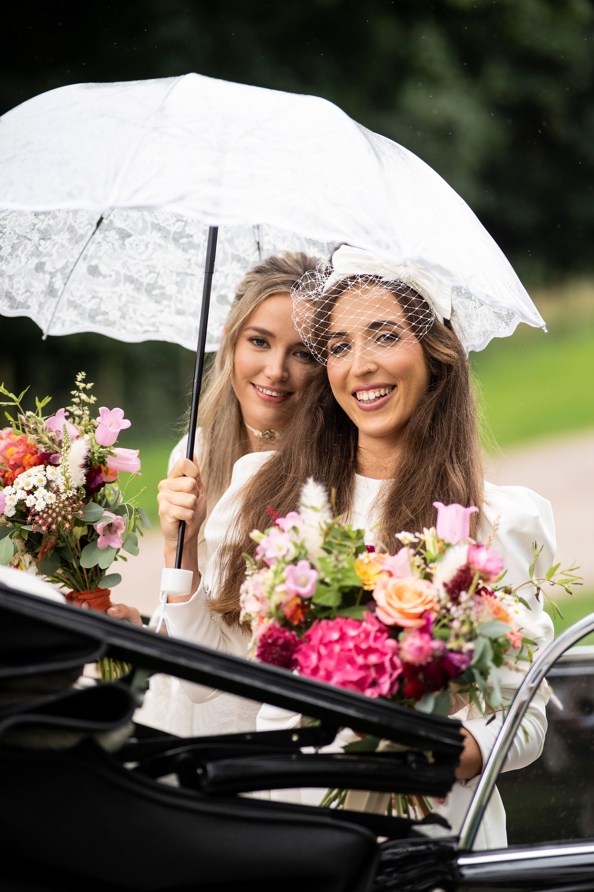 Two brides smiling under an umbrella