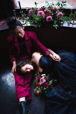 Married couple on floor in front of window and wedding florals