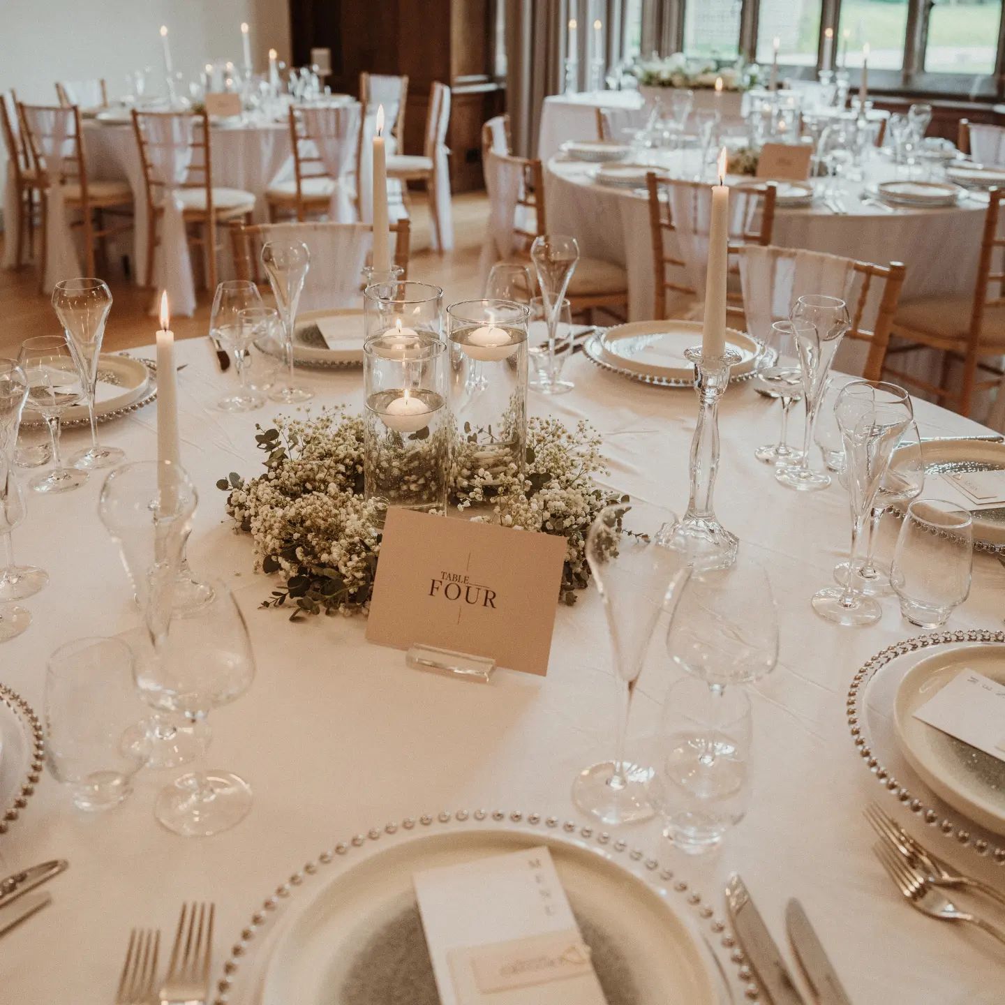 A round table styled for a wedding, with cutlery, glasses, candles and gypsophila and eucalyptus centrepiece