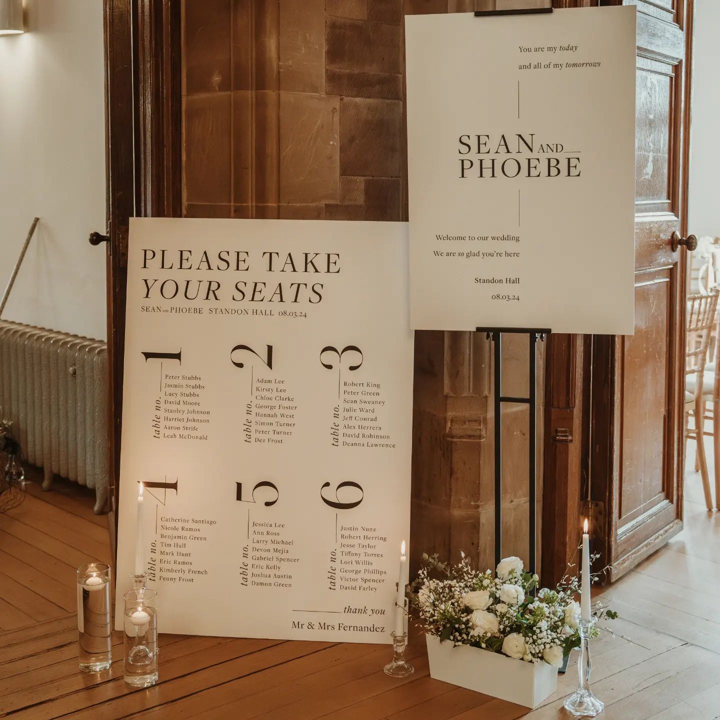 A wedding welcome sign and seating chart, decorated with candles and flowers  