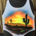 A desert sunset and cactus airbrushed on a shirt. Airbrush on white apparel. An Arizona desert scene sunset in contrast to the wet pool or beach where the swimsuit will be worn.