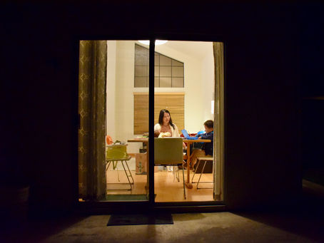 A woman breastfeeding a baby while watching a young child doing homework