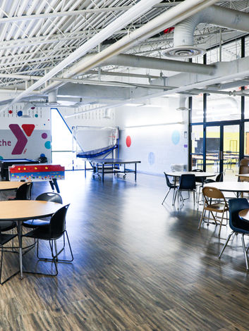 Spacious YMCA community room with "the Y" logo, tables, chairs, and games.