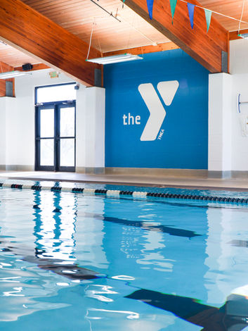 Indoor swimming pool with lane lines and 'the Y' logo on wall.