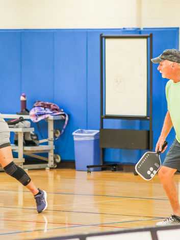 Two active men playing pickleball indoors on a wooden court.