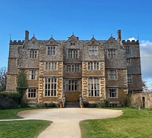 The grand Jacobean façade of Chastleton House, a well-preserved 17th-century manor in the Cotswolds, surrounded by lush gardens and historic stone walls.
