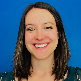 Headshot of Ally Joel, adaptive assessor, a white woman in her thirties, with shoulder length brown hair against a blue wall.