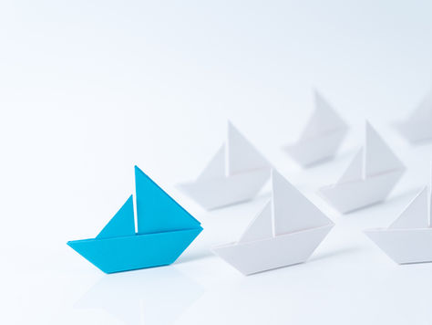 Blue oragami sailing boat leading a fleet of white boats - representing leadership