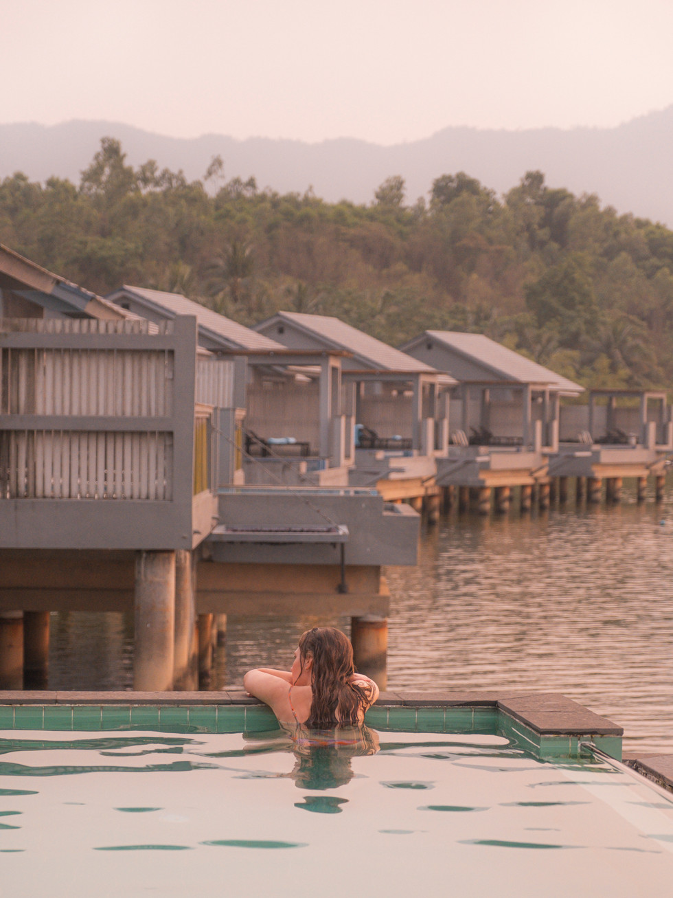 junge Frau lehnt am Rand eines Pools einer Wasservilla und genießt den Sonnenuntergang, Hue, Vietnam