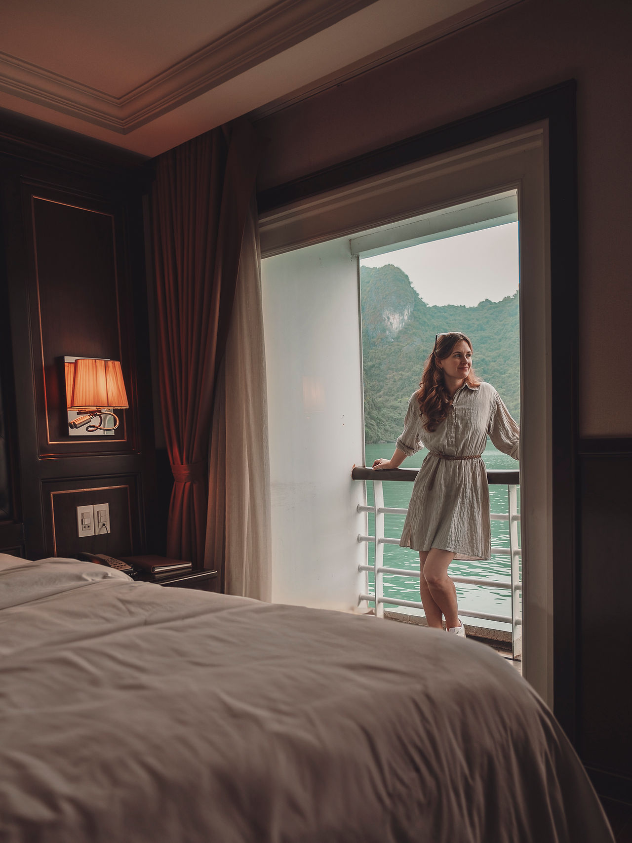 Frau auf Kreuzfahrtschiff blickt aus dem Balkon auf die Landschaft der Halongbucht, Vietnam