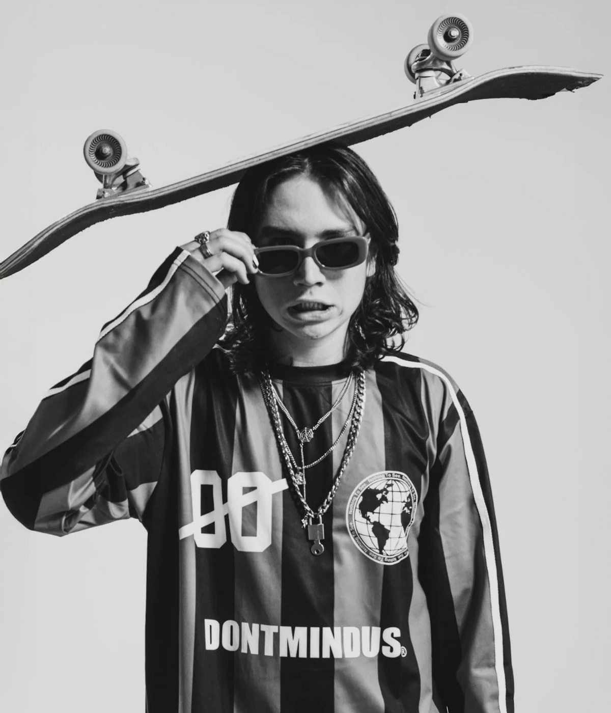 TJ Minor in black-and-white, sunglasses on, holding a skateboard over his head