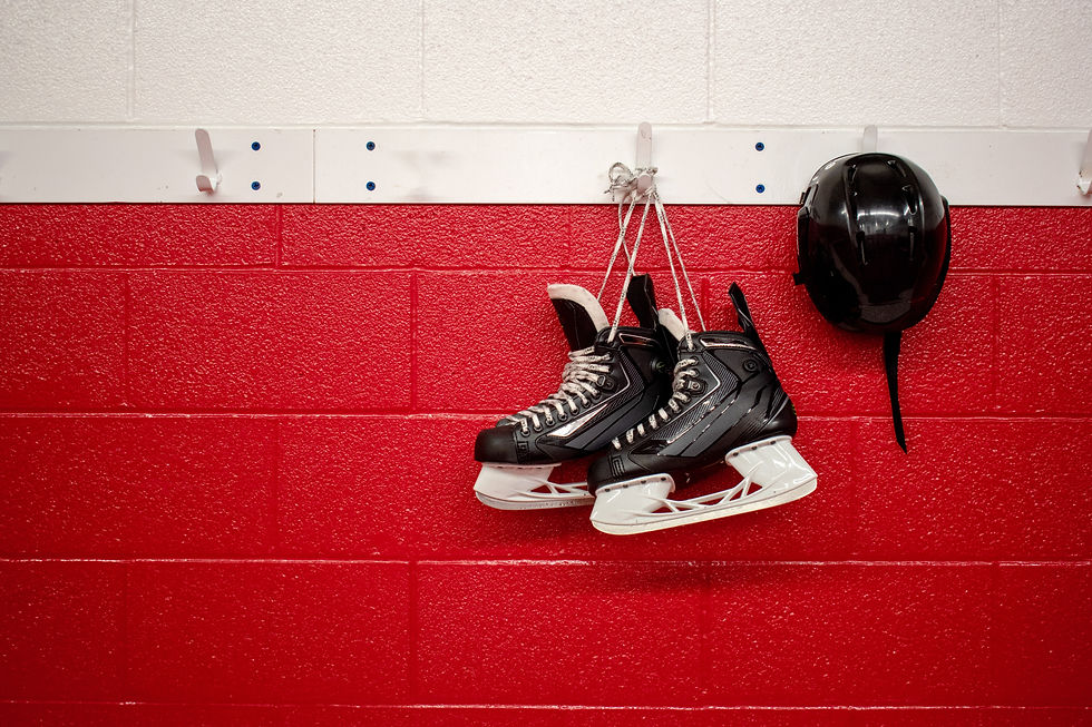 Hockey skates and a helmet are hanging from hooks on a white and red cinderblock wall.