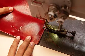italian artisan sewing a red leather wallett in florence.webp