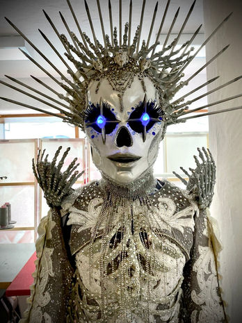 Figur in Skelett-Kostüm mit stacheliger Krone und leuchtend blauen Augen.