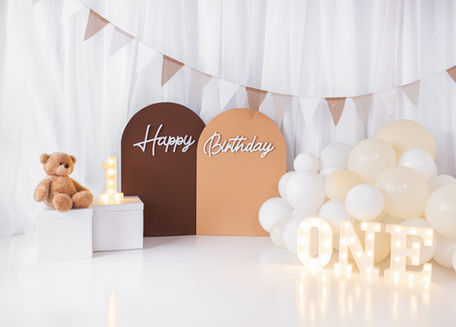 Neutral white smash cake birthday setup with balloons, arches, and ONE letters in a professional studio in Houston