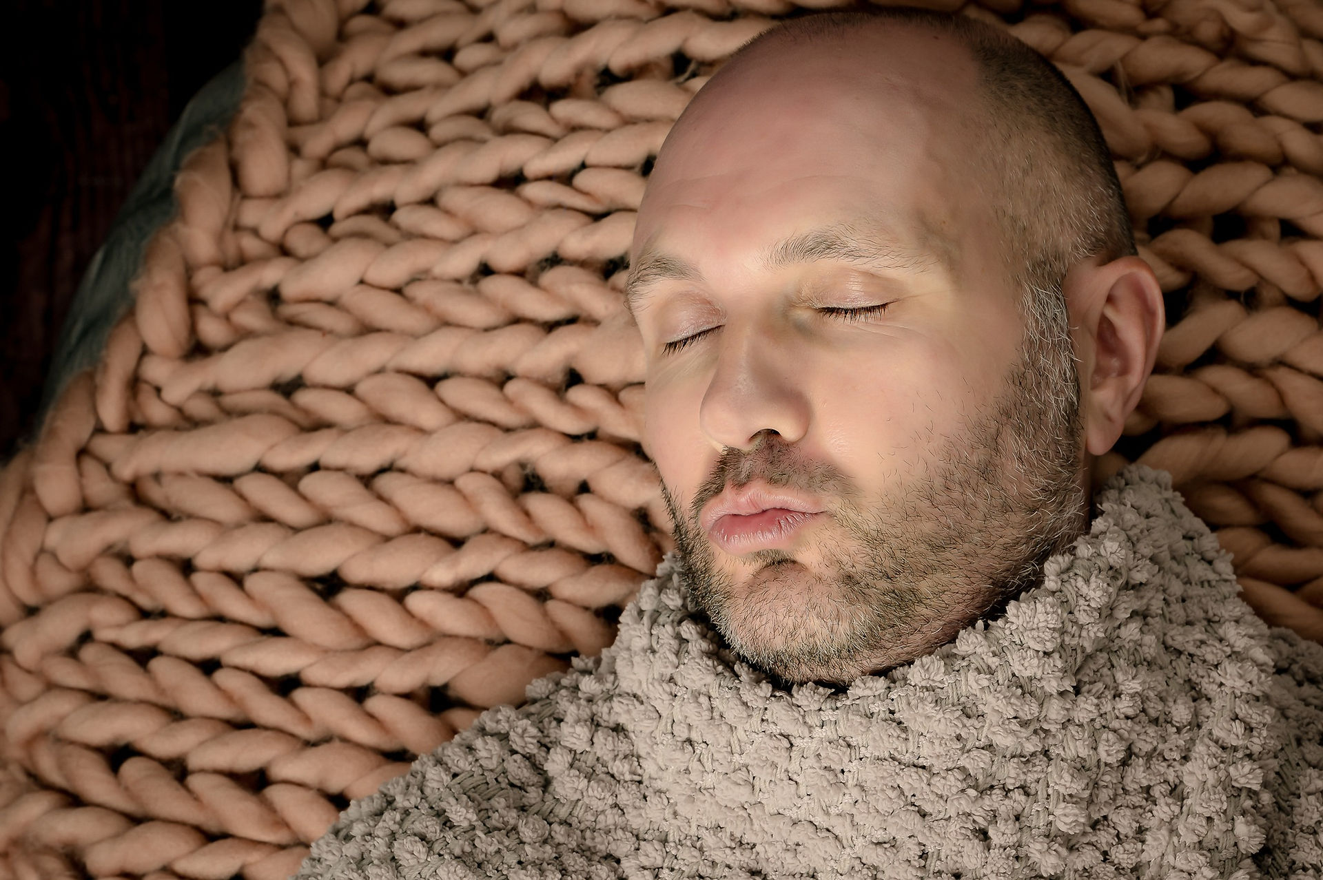 adult-man-coping-newborn-pose-lying-on-bean-bag-wrapped-in-blankets