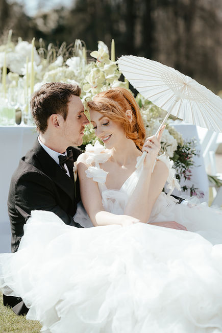The bride and groom sat on the grass next to their table under an umbrella