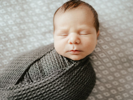 Newborn baby sleeping peacefully, wrapped in a textured gray blanket on a patterned gray background, conveying calm and serenity.