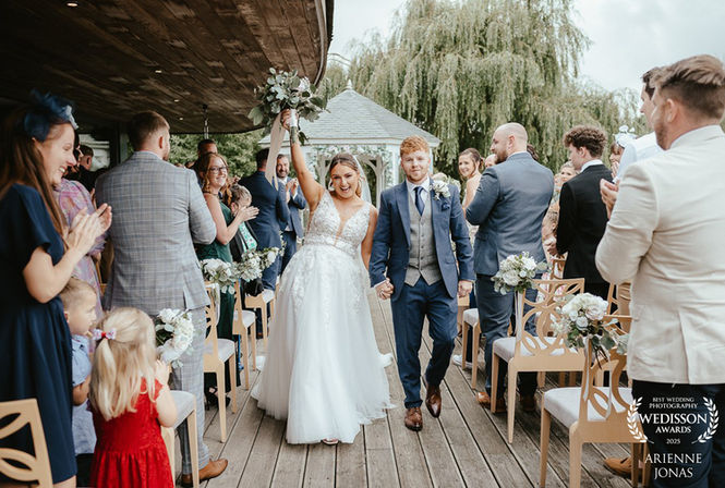 bride and groom walking down the alise at the boat house norfolk bride arm up in the air celebrating
