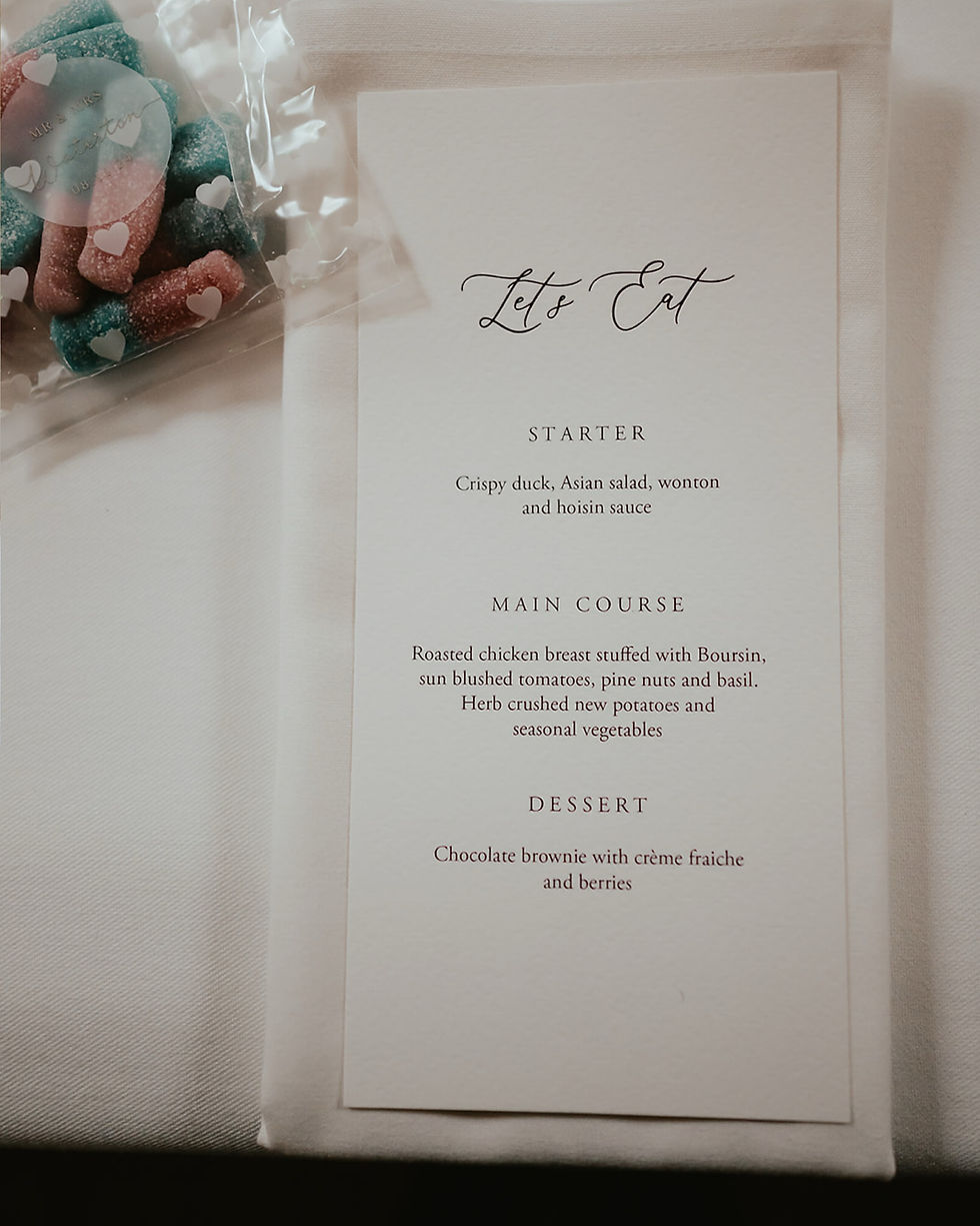 Wedding menu on a table with starter, main course, and dessert details. Bag of colorful heart-shaped candy is beside it.