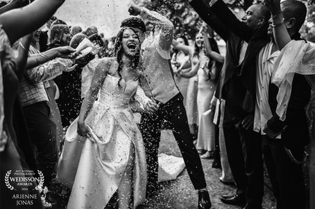 Bride and groom joyfully walk through guests throwing confetti, set outdoors. Black and white, festive, with "Wedisson Awards 2024" text.