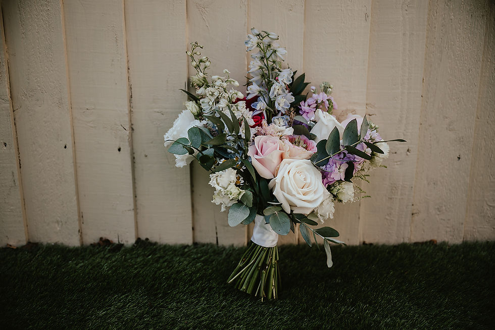 Bouquet of pink, white, and purple flowers with greenery against a wooden wall and grass, conveying a fresh, rustic charm.