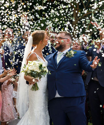 Newlyweds celebrate as guests toss white confetti over them.