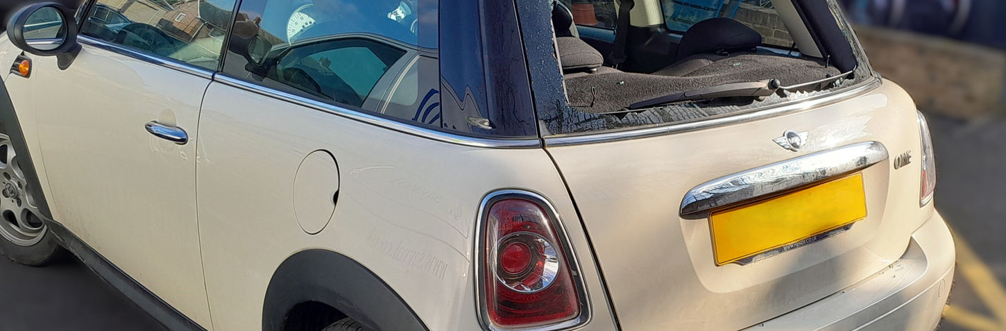 A 2012 Mini One with a shattered rear windscreen parked in Ealing, W5, requiring a heated rear window replacement by My Car Glass Ltd. The vehicle is captured in daylight, emphasizing the extent of the damage and the need for professional auto glass repair. 